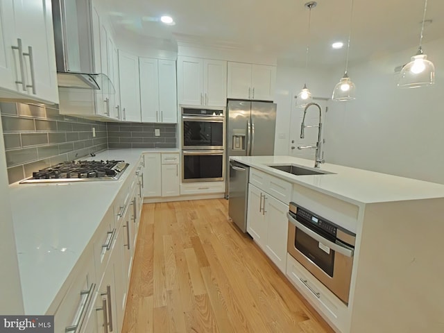 kitchen featuring appliances with stainless steel finishes, pendant lighting, white cabinetry, sink, and light hardwood / wood-style floors