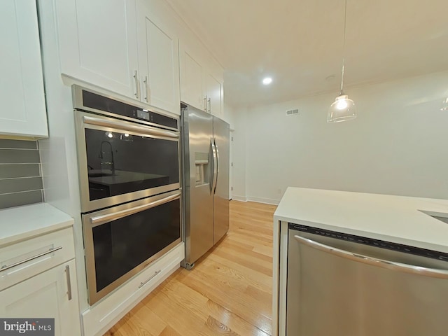 kitchen with white cabinetry, appliances with stainless steel finishes, light wood-type flooring, and pendant lighting