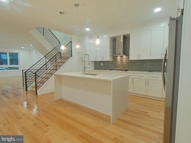 kitchen featuring decorative light fixtures, stainless steel refrigerator, wall chimney range hood, black gas stovetop, and white cabinets