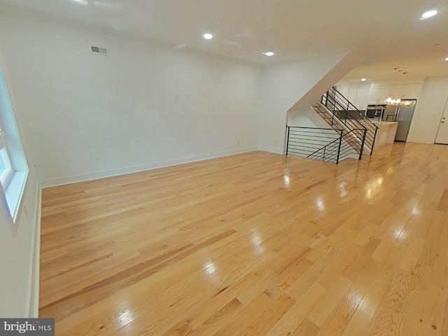 unfurnished living room featuring an inviting chandelier and light hardwood / wood-style floors