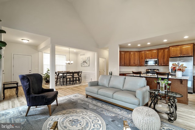 living room featuring high vaulted ceiling, light hardwood / wood-style floors, and a notable chandelier