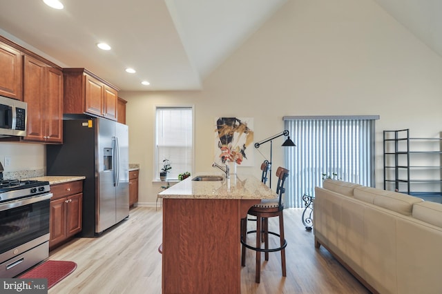 kitchen with appliances with stainless steel finishes, a breakfast bar, sink, light hardwood / wood-style floors, and an island with sink