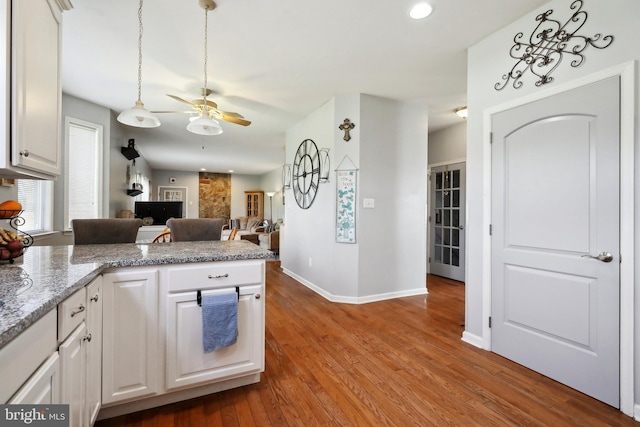 kitchen featuring hardwood / wood-style flooring, ceiling fan, light stone countertops, and white cabinetry