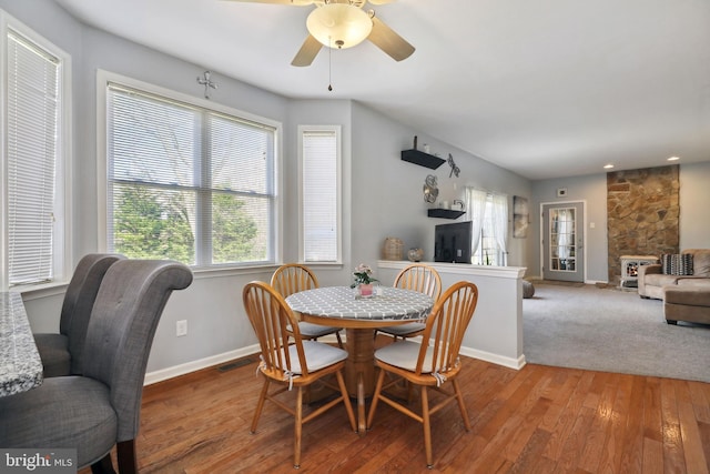 dining space featuring light hardwood / wood-style floors, a stone fireplace, and ceiling fan