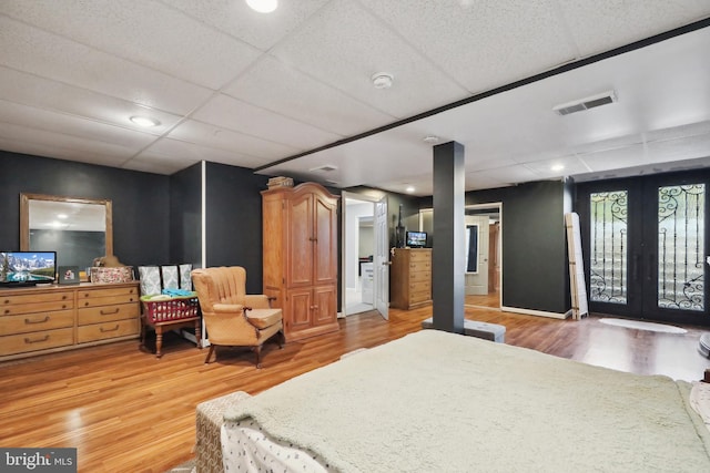 bedroom featuring a drop ceiling, light wood-type flooring, and french doors