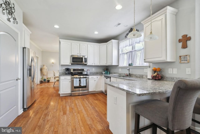 kitchen with white cabinetry, stainless steel appliances, kitchen peninsula, decorative light fixtures, and light wood-type flooring