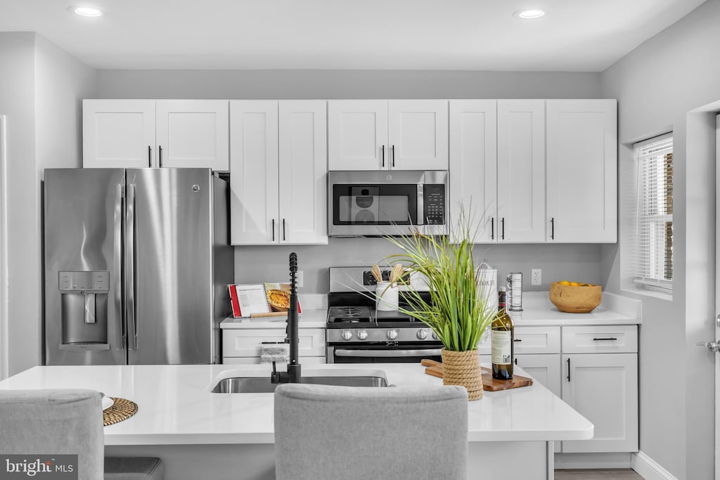 kitchen with a kitchen bar, appliances with stainless steel finishes, white cabinetry, and an island with sink