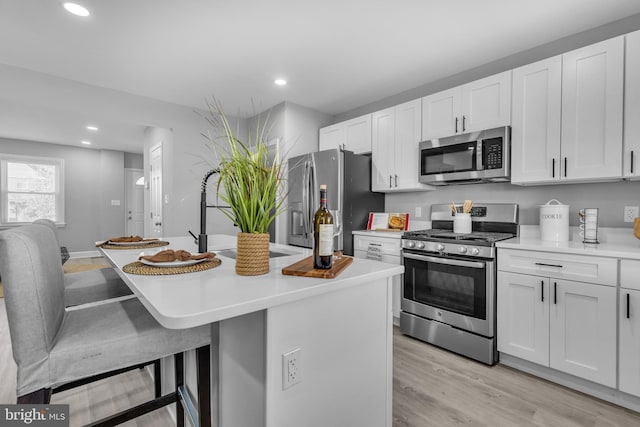 kitchen with white cabinetry, stainless steel appliances, an island with sink, light hardwood / wood-style floors, and a breakfast bar