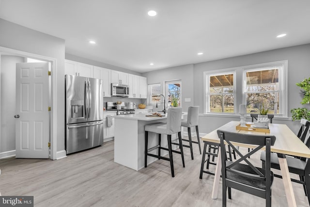 kitchen featuring white cabinetry, a breakfast bar, stainless steel appliances, and light wood-type flooring