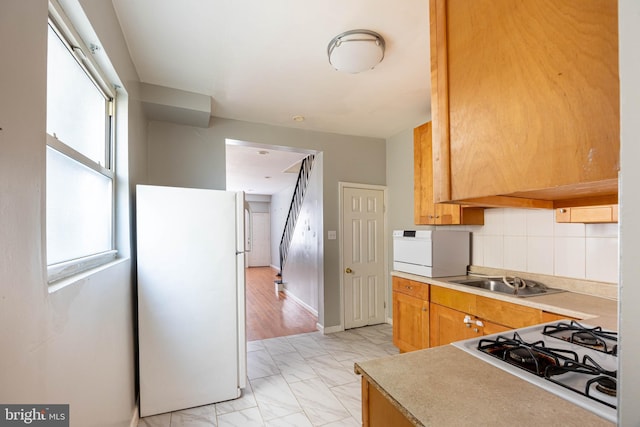 kitchen with decorative backsplash, white appliances, sink, and light hardwood / wood-style flooring