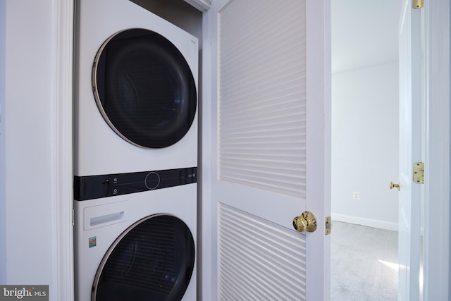 washroom with stacked washer and dryer, laundry area, carpet floors, and baseboards