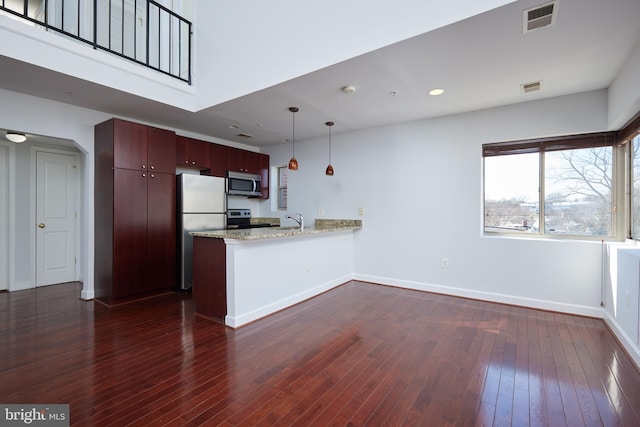 kitchen featuring light stone counters, a peninsula, appliances with stainless steel finishes, dark wood finished floors, and pendant lighting