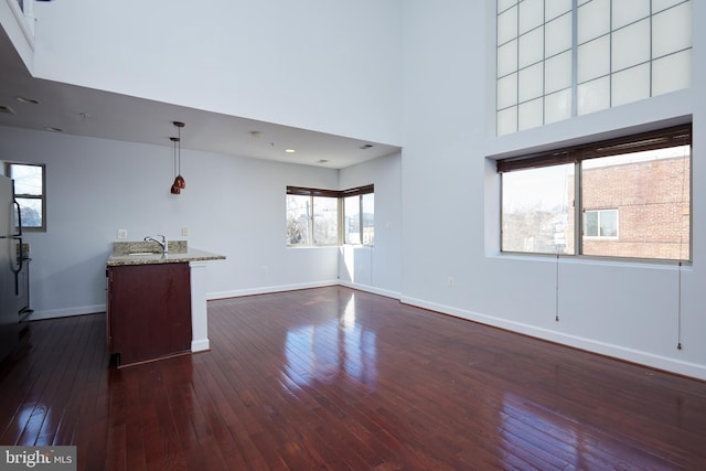 unfurnished living room featuring dark wood-style floors, a high ceiling, a sink, and baseboards