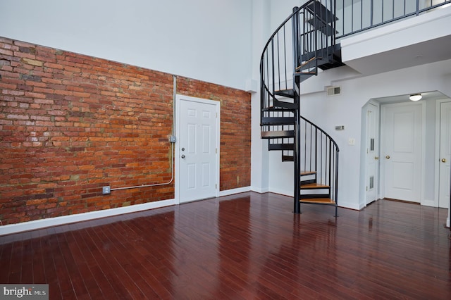 foyer entrance with visible vents, a towering ceiling, dark wood-type flooring, brick wall, and baseboards