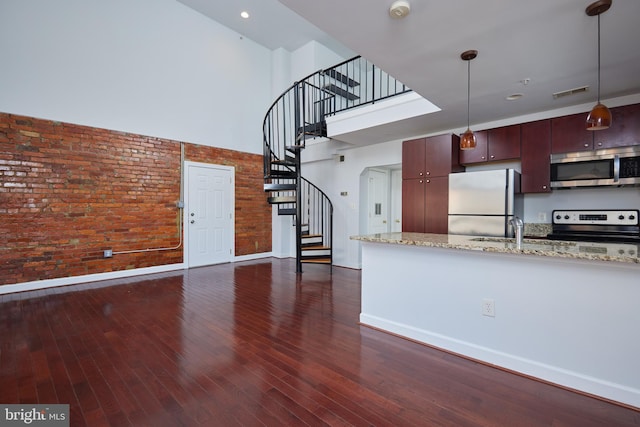 kitchen with dark wood finished floors, light stone counters, hanging light fixtures, a high ceiling, and stainless steel appliances