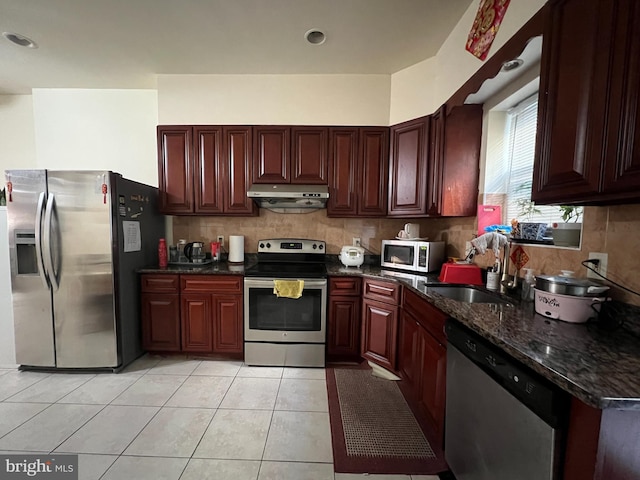 kitchen featuring sink, dark stone counters, decorative backsplash, light tile patterned flooring, and appliances with stainless steel finishes