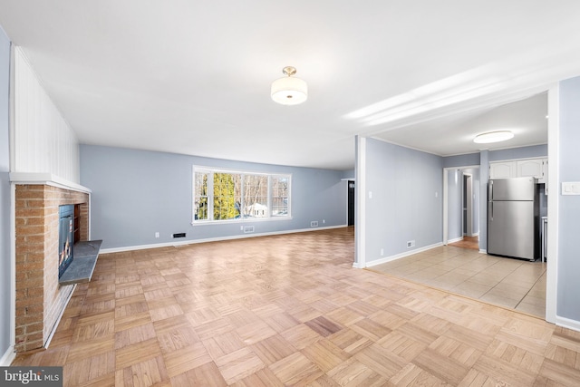 unfurnished living room featuring a brick fireplace and light parquet floors