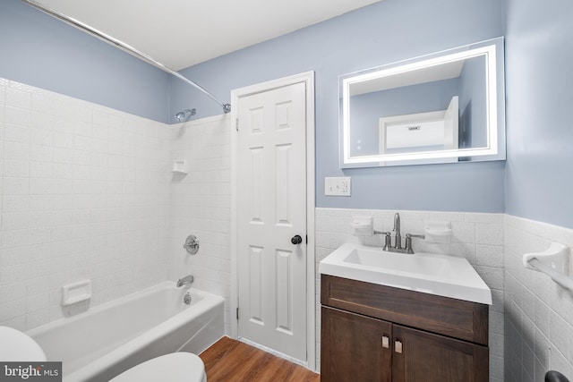 full bathroom featuring vanity, wood-type flooring, tile walls, toilet, and tiled shower / bath