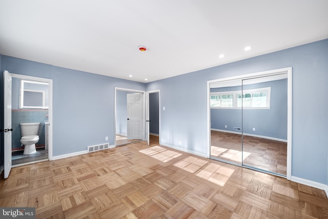 unfurnished bedroom with light parquet floors, tile walls, and ensuite bath