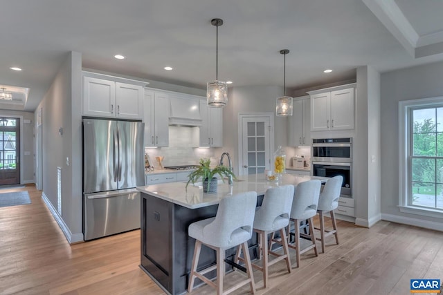 kitchen featuring white cabinets, a center island with sink, stainless steel appliances, and light hardwood / wood-style flooring