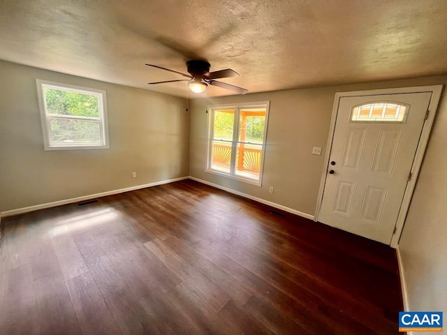 foyer entrance with a textured ceiling, dark wood-type flooring, ceiling fan, and a healthy amount of sunlight