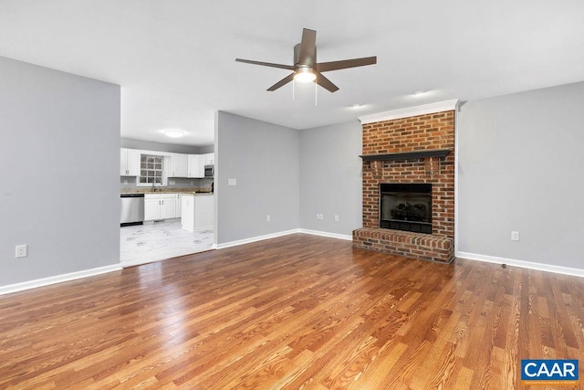 unfurnished living room featuring ceiling fan, light hardwood / wood-style flooring, sink, and a brick fireplace