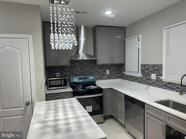 kitchen featuring appliances with stainless steel finishes, backsplash, wall chimney exhaust hood, sink, and gray cabinets