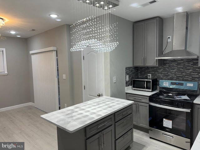 kitchen featuring a center island, wall chimney range hood, gray cabinets, light wood-type flooring, and stainless steel appliances