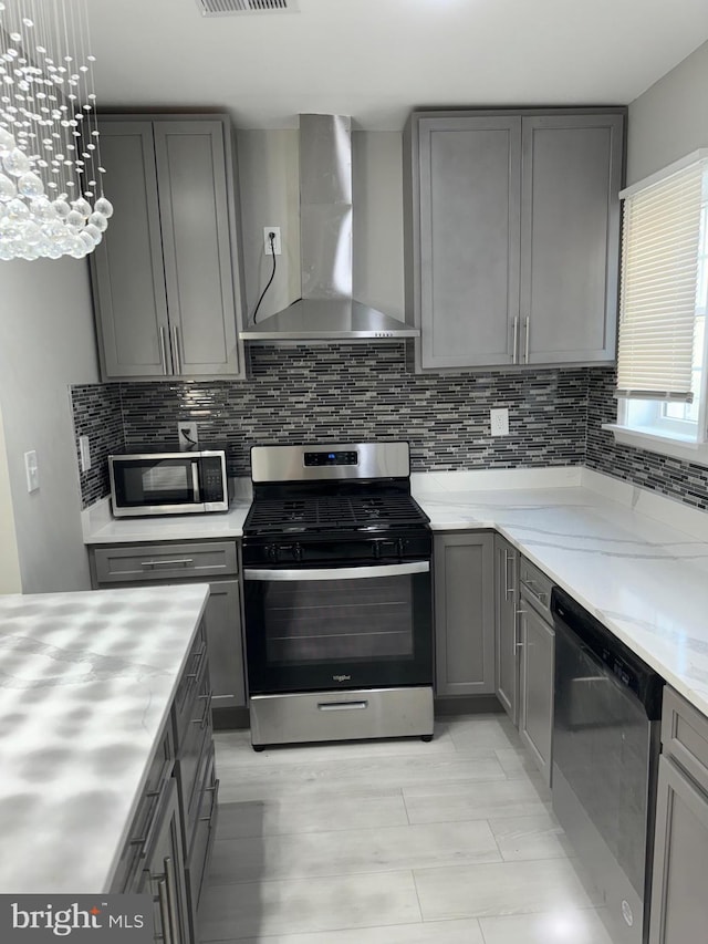 kitchen with wall chimney exhaust hood, gray cabinets, decorative backsplash, and appliances with stainless steel finishes