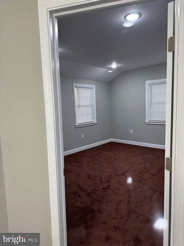 empty room featuring dark carpet and vaulted ceiling