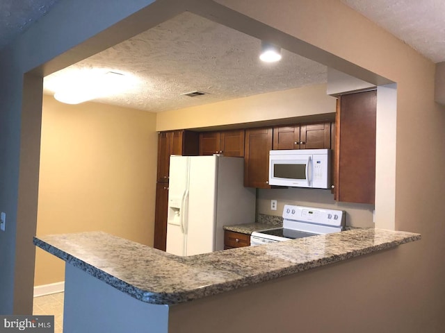 kitchen featuring white appliances, light tile patterned floors, a textured ceiling, stone countertops, and kitchen peninsula