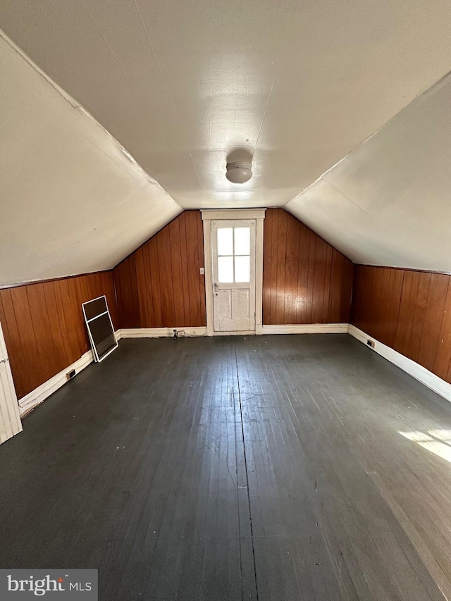 additional living space featuring wooden walls, dark wood-type flooring, and lofted ceiling