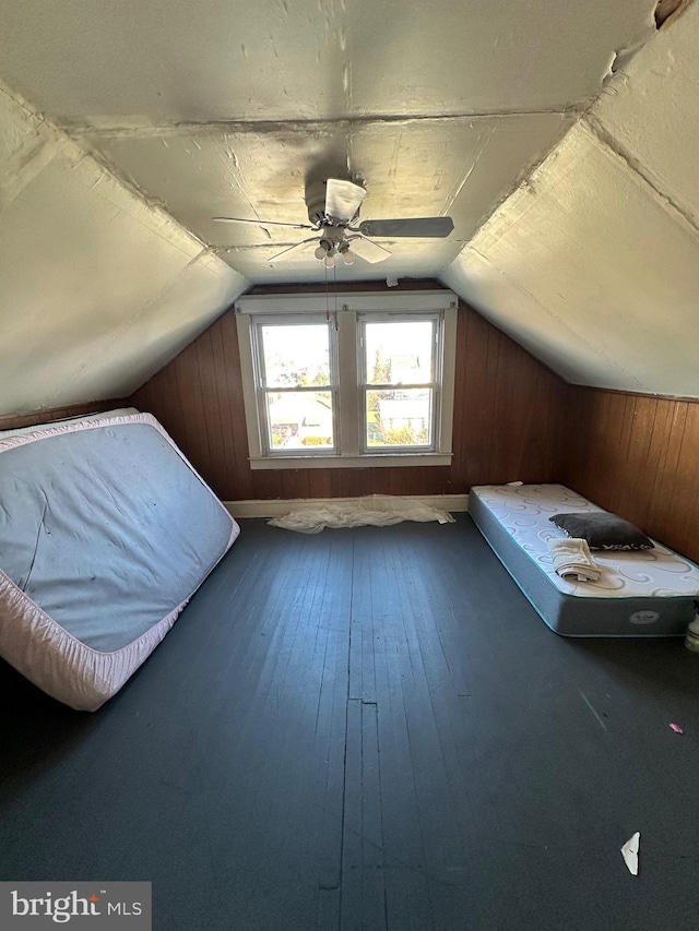 unfurnished bedroom featuring ceiling fan, wood-type flooring, wooden walls, and lofted ceiling