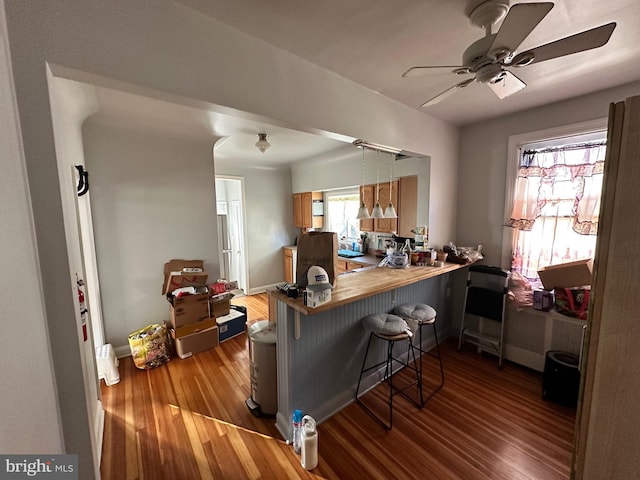 kitchen featuring a kitchen breakfast bar, kitchen peninsula, ceiling fan, and light hardwood / wood-style flooring