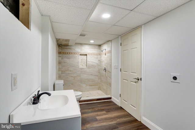 bathroom featuring hardwood / wood-style floors, tiled shower, a paneled ceiling, toilet, and vanity