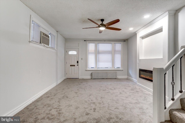 unfurnished living room featuring ceiling fan, radiator heating unit, cooling unit, light colored carpet, and a textured ceiling