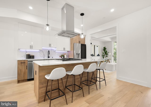 kitchen with island range hood, stainless steel appliances, pendant lighting, light hardwood / wood-style flooring, and white cabinets