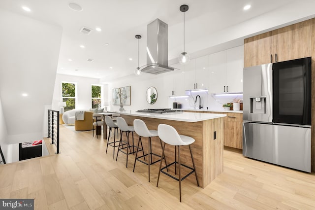 kitchen featuring hanging light fixtures, island exhaust hood, light hardwood / wood-style floors, white cabinets, and appliances with stainless steel finishes