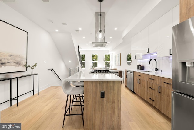 kitchen featuring white cabinetry, light hardwood / wood-style flooring, pendant lighting, a kitchen island, and appliances with stainless steel finishes