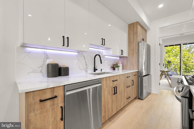 kitchen featuring white cabinetry, sink, light stone countertops, light hardwood / wood-style flooring, and appliances with stainless steel finishes