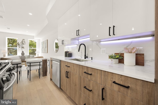 kitchen featuring white cabinetry, sink, stainless steel appliances, light stone counters, and light wood-type flooring