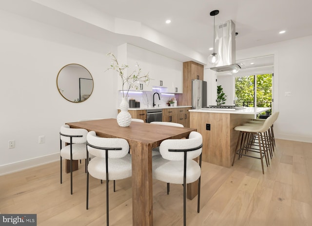 kitchen featuring island exhaust hood, kitchen peninsula, stainless steel appliances, pendant lighting, and light hardwood / wood-style floors