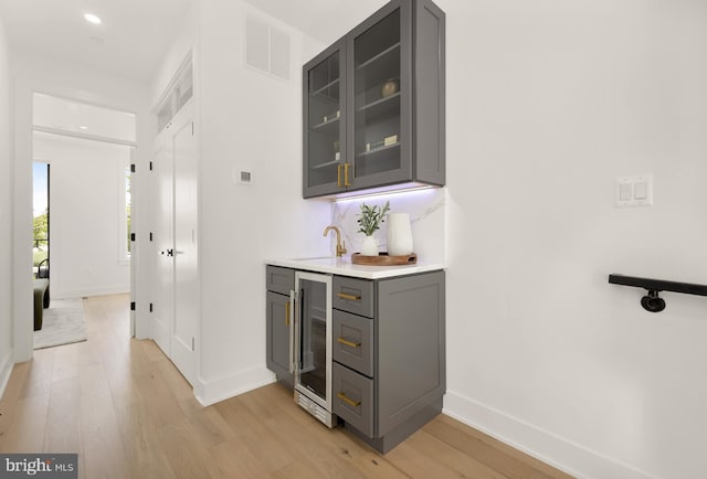 bar with gray cabinetry, light wood-type flooring, sink, and wine cooler