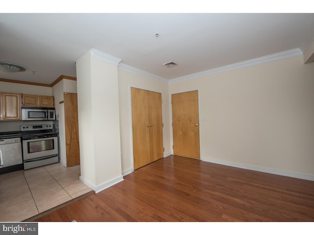 kitchen featuring light tile patterned floors, light brown cabinetry, crown molding, and appliances with stainless steel finishes