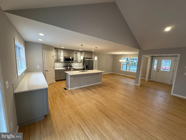 kitchen with gray cabinetry, stainless steel appliances, a kitchen island with sink, light hardwood / wood-style flooring, and hanging light fixtures