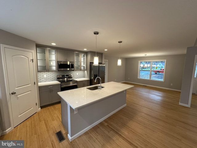 kitchen with appliances with stainless steel finishes, sink, decorative light fixtures, a center island with sink, and light hardwood / wood-style floors