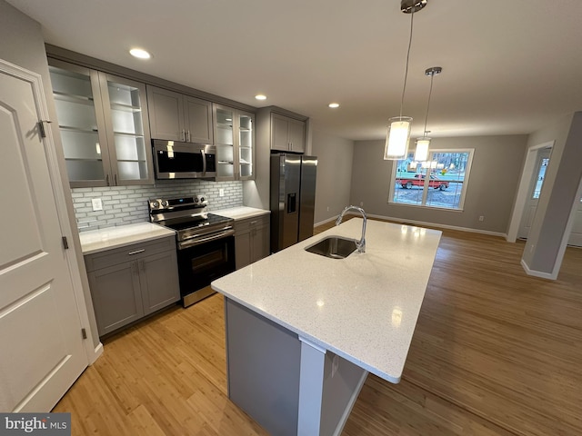 kitchen with stainless steel appliances, a kitchen island with sink, sink, pendant lighting, and light hardwood / wood-style floors