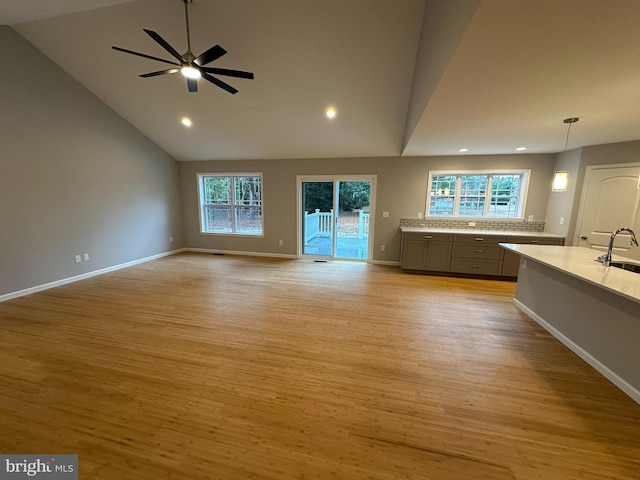 unfurnished living room with ceiling fan, plenty of natural light, high vaulted ceiling, and light hardwood / wood-style flooring