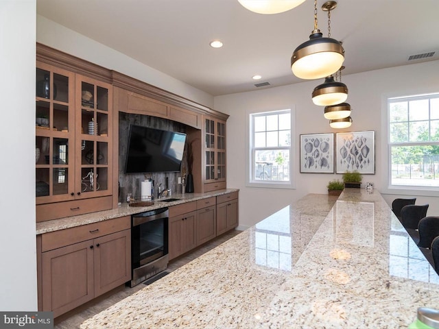 kitchen with light stone counters, sink, beverage cooler, and pendant lighting