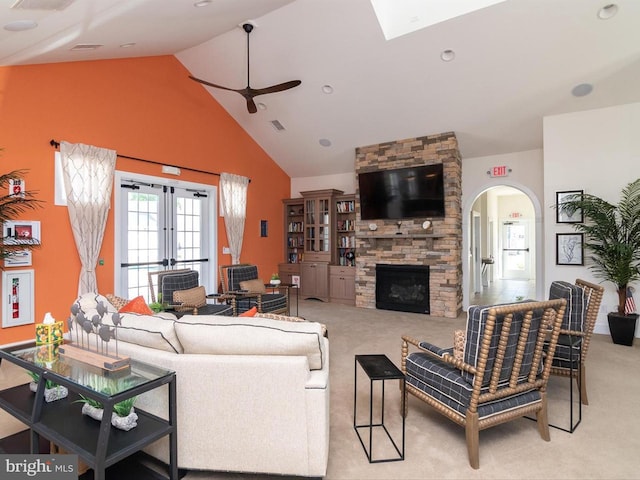 carpeted living room featuring a stone fireplace, ceiling fan, french doors, and high vaulted ceiling